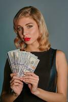 blond flicka i svart klänning innehav en fläkt av hundra dollar räkningar , Framställ mot grå bakgrund. hasardspel underhållning, poker, kasino. närbild. foto