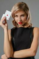 blond flicka i svart eleganta klänning som visar två spelar kort, Framställ mot grå bakgrund. hasardspel underhållning, poker, kasino. närbild. foto