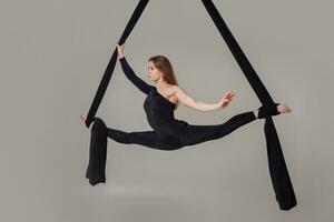 skön flicka i en svart sport kostym är utför ett akrobatisk element i en studio. foto