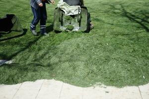 skärande gräs med maskin arbetstagare trimning trädgård med gräsklippare foto