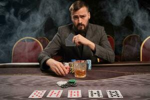 stilig skäggig man är spelar poker Sammanträde på de tabell i kasino. foto