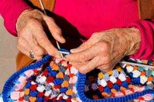 ett äldre kvinna är stickning en färgrik virka filt foto