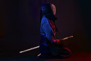 stänga upp skott, kendo kämpe bär i ett rustning, traditionell kimono, hjälm praktiserande krigisk konst med shinai bambu svärd, svart bakgrund. foto