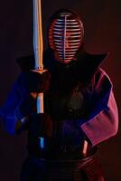 stänga upp skott, kendo kämpe bär i ett rustning, traditionell kimono, hjälm praktiserande krigisk konst med shinai bambu svärd, svart bakgrund. foto