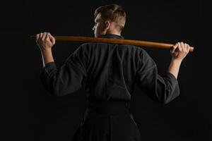 kendo guru bär i en traditionell japansk kimono är praktiserande krigisk konst med de shinai bambu svärd mot en svart studio bakgrund. foto