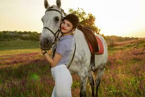 jockey ung flicka petting och kramas vit häst i kväll solnedgång foto