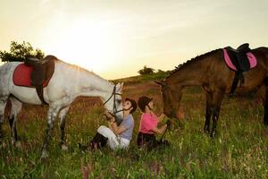två kvinna och två hästar utomhus- i sommar Lycklig solnedgång tillsammans natur foto