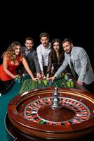 grupp av ung människor Bakom roulett tabell i en kasino foto