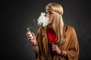 porträtt av sexig ung hipster rökning vaping flicka. de kvinna är klädd i de stil av en boho. ånga begrepp. vaping e-cigarett. foto