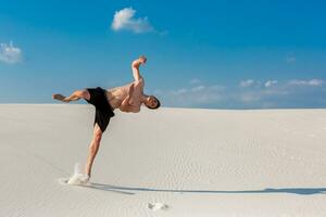 porträtt av ung parkour man håller på med flip eller kullerbytta på de sand. foto