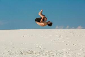 ung man Hoppar på de strand med vit sand och ljus blå himmel foto