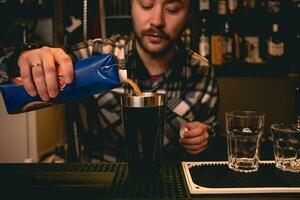 skäggig bartender häller orange juice från kartong till shaker, framställning cocktail foto