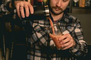 bartender häller cocktail från shaker in i lång glas med is foto
