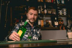 självsäker skäggig bartender häller grön sprit från flaska in i skott glas foto