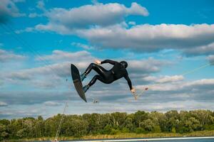 idrottare Hoppar med baksida rotation på wakeboard över vatten yta i sommar dag foto