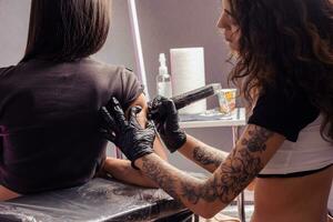 fokuserade flicka tatuerare skapande tatuering med text på ärm av kvinna foto