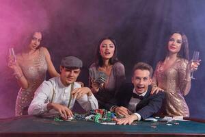 vänner spelar poker på kasino, på tabell med stackar av pommes frites, pengar, kort på Det. fira vinna, leende. svart, rök bakgrund. närbild. foto