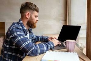 ung man chattar via nätbok under arbete ha sönder i kaffe affär, manlig Sammanträde i främre öppen bärbar dator dator med tom kopia Plats skärm. foto