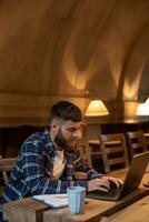 ung professionell surfing de internet på hans bärbar dator i en Kafé foto