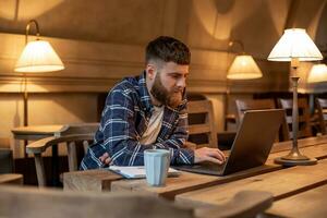 ung professionell surfing de internet på hans bärbar dator i en Kafé foto