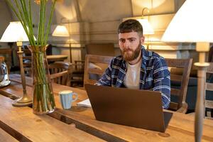 ung professionell surfing de internet på hans bärbar dator i en Kafé foto