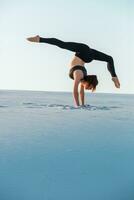 ung kvinna praktiserande inversion balansering yoga utgör stå på händer på sand. foto