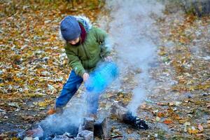 en barn sätter ut en brand efter en picknick i de höst skog foto