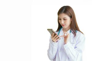 professionell ung asiatisk kvinna läkare bär vit morgonrock och stetoskop medan använder sig av smartphone till kommunicera med patienter medan isolerat på vit bakgrund. foto