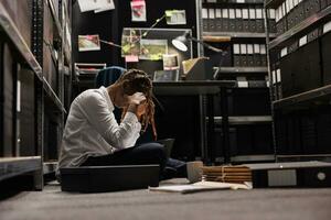 kvinna forskare lidande från migrän medan lösning brottslighet på detektiv- kontor golv. utmattad överarbetad lag tillämpning ombud med huvudvärk analyserar bevis på natt tid foto