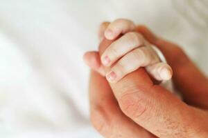 stänga upp Foto av far innehav nyfödd bebis hand.