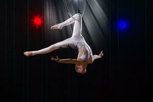 utför en cirkus flicka skådespelerska. cirkus antenn gymnast på de ring. akrobatik. tonåring utför ett akrobatisk lura i de luft foto