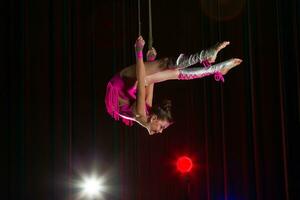 cirkus konstnär akrobat prestanda. de flicka utför akrobatisk element i de luft. cirkus gymnast på de skede foto