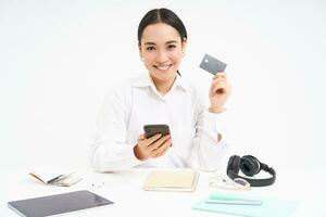 företags- och företag. asiatisk kvinna i kontor, innehar smartphone och kreditera kort, betalande uppkopplad, miljö upp direkt debitera uppkopplad, vit bakgrund foto