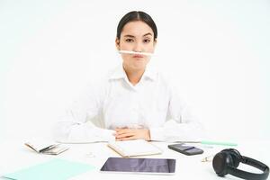företag och kontor arbete. ung kvinna Sammanträde på arbetsplats, lurar runt om, innehar penna med mun och visar rolig ansikten, vit bakgrund foto