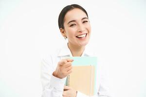 porträtt av leende japansk kvinna, innehar pappersarbete, poäng på kamera och skrattar, inviterar till henne kurser, vit bakgrund foto