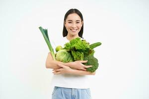 bild av leende asiatisk kvinna med grönsaker, äter friska grön organisk mat, isolerat på vit bakgrund foto