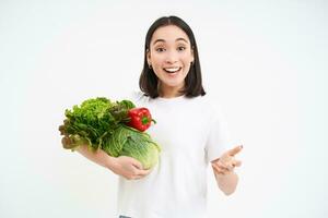 entusiastisk vegetarian flicka, innehav grön grönsaker och leende, rekommenderar näringsrik organisk mat, vit bakgrund foto