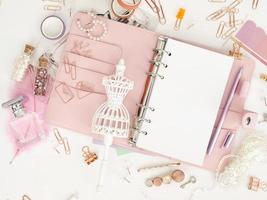ovanifrån av en rosa planerare med söta brevpapper. rosa glamourplanerare med en vit skyltdocka. planerare med öppna sidor på en vit bakgrund och med vackra tillbehörspennor, knappar, stift. foto