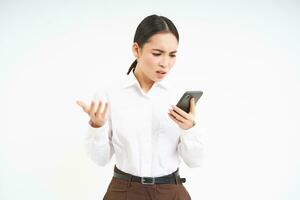 koreanska affärskvinna utseende förvirrad och frustrerad på smartphone skärm, läser konstig meddelande på henne telefon med förbryllad ansikte, axelryckningar axlar foto