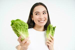 friska diet och organisk mat. leende asiatisk kvinna som visar kål, äter sallad, rensning henne kropp, på detox, vit bakgrund foto