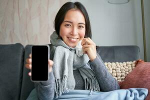 upphetsad ung kvinna pekande finger på smartphone, som visar uppkopplad läkare, medicinsk Ansökan eller gp Kontakt på mobil telefon, vistas på Hem sjuk, fångst kall foto