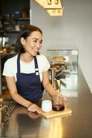 vertikal skott av leende asiatisk Barista, flicka arbetssätt i Kafé, ger beställa till klient, tillverkad omgång brygga, filtrera kaffe foto