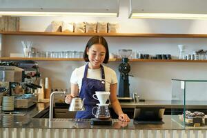 leende asiatisk flicka Barista, arbetssätt i Kafé, bryggning kaffe v60, framställning beställa Bakom disken foto