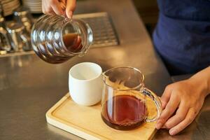 stänga upp av kvinna Barista händer häller filtrera kaffe in i kopp, framställning beställa för Kafé klient foto