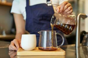 stänga upp av glas burk och en kopp stående på Kafé disken, Barista häller filtrera kaffe och framställning beställa foto