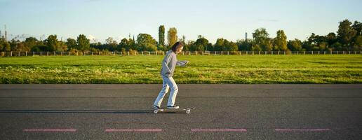 hobbies och livsstil. ung kvinna ridning skateboard. skater flicka njuter kryssning på longboard på solig dag utomhus foto