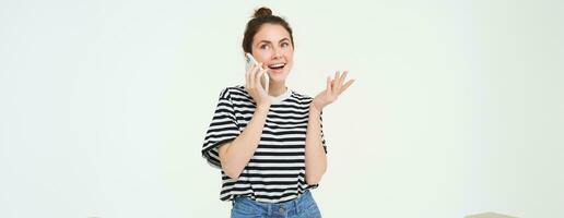 Lycklig ung kvinna samtal på mobil telefon, chatt på telefon, användningar smartphone, står över vit bakgrund foto