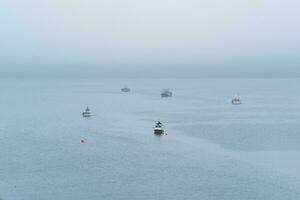 fiske båtar på hav mot de bakgrund av en avlägsen dimmig kust foto