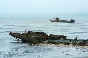 resterna av en förstört fartyg på en dimmig havsstrand foto