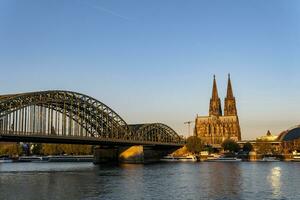 cologne katedral och hohenzollern bro upplyst förbi de morgon- Sol foto